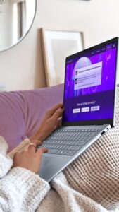 A close-up shot of a person using a silver Windows Dell laptop while relaxing on a couch, with the screen displaying an AI assistant interface.