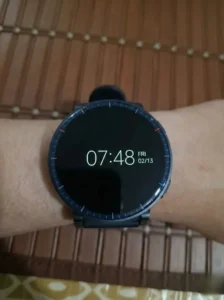 Amazfit Active 3 Premium smartwatch worn on wrist, displaying a minimalist black watch face with digital time (07:48) and date (Fri 02/13), set against a wooden background.