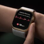 Close-up of a gold smartwatch on a wrist displaying a “Diabetes Risk Scan” screen with an ECG waveform, the message “Analyzing vascular patterns…” and a heart rate reading of 78 bpm.